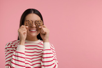 Young woman with chocolate chip cookies on pink background, space for text