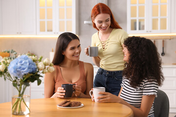 Happy young friends with cups of drink spending time together in kitchen