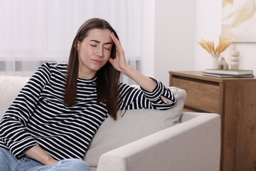 Sad woman suffering from headache on sofa indoors