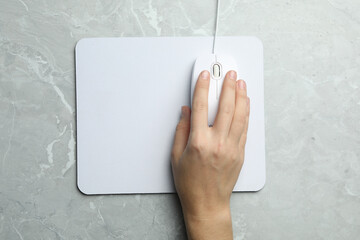 Woman using wired computer mouse on light grey marble table, top view. Space for text