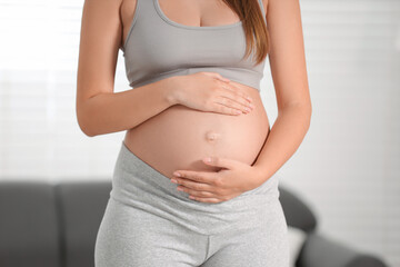Pregnant woman standing near sofa at home, closeup