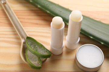 Different lip balms and aloe vera plant on wooden table, closeup - obrazy, fototapety, plakaty