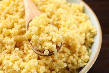 Tasty millet porridge and spoon in bowl on table, closeup