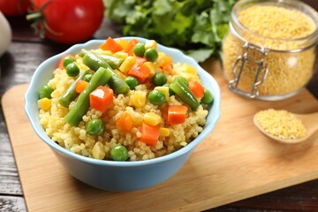 Tasty millet porridge with vegetables in bowl on wooden table, closeup