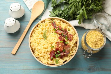 Tasty millet porridge with bacon, green onion and dill in bowl served on light blue wooden table, flat lay