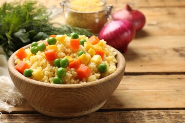 Tasty millet porridge with vegetables in bowl on wooden table, closeup. Space for text