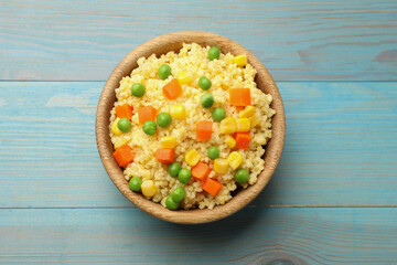 Tasty millet porridge with vegetables in bowl on light blue wooden table, top view