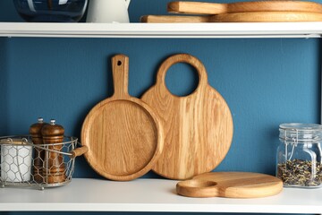 Wooden cutting boards, kitchen utensils and dry tea on shelving unit near blue wall