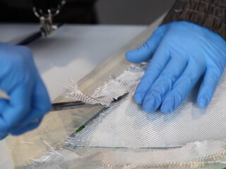Hands in protective gloves cutting with scissors when Fiberglass products production process of...