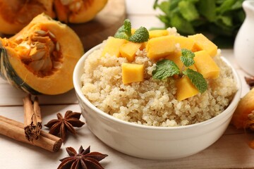 Tasty quinoa porridge with pumpkin, mint in bowl and spices on light wooden table, closeup