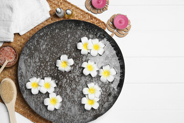 Bowl of water with flowers and different spa supplies on white wooden table, top view. Space for text