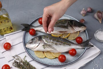 Woman adding spices onto raw dorado fish at grey table, closeup