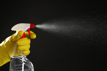 Woman spraying liquid from bottle on black background, closeup