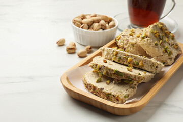 Tasty halva with pistachios served on white marble table, closeup. Space for text