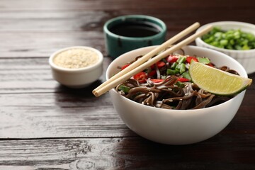Tasty buckwheat noodles (soba) with chili pepper and lime served on wooden table, closeup. Space for text
