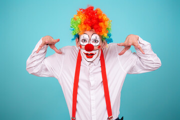 A joyful clown. A cute man in a suit and makeup for a holiday for children. A fool. Blue background. Copy the space.