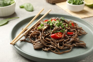 Tasty buckwheat noodles (soba) with chili pepper, onion and chopsticks on light table, closeup