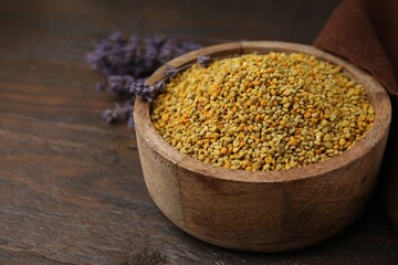 Fresh bee pollen granules in bowl and lavender on wooden table, closeup. Space for text