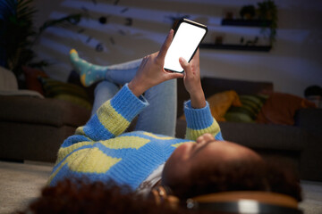 Unrecognizable teenage girl lying on living room carpet using mobile, blank empty screen. Black gen...