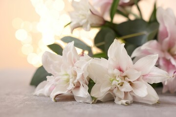 Bouquet of beautiful lily flowers on table against beige background with blurred lights, closeup