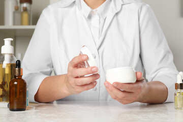 Dermatologist holding jar of cream at white table indoors, closeup. Developing cosmetic product
