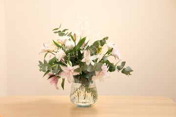 Bouquet of beautiful lily flowers in vase on wooden table against beige background