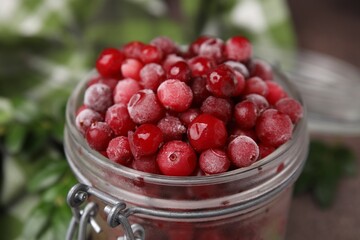 Frozen red cranberries in glass jar on table, closeup