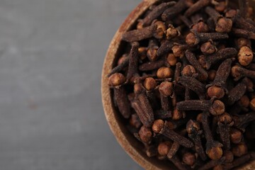 Aromatic cloves in bowl on grey table, top view. Space for text