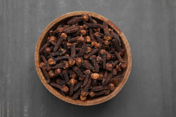 Aromatic cloves in bowl on grey wooden table, top view