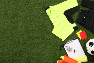 Uniform, soccer ball and other referee equipment on green grass, flat lay. Space for text