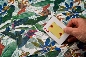Hand holding a poker card of the two of hearts on a tropical background. Concept luck in love.
