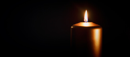 Candle burning in darkness over black background