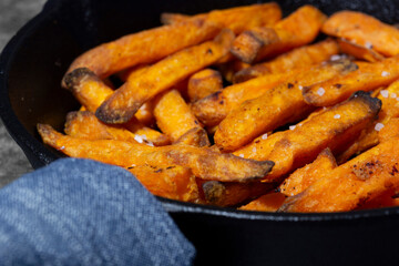 Sweet potato fries cooked in a cast iron frying pan. On a dark stone background