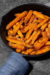 Sweet potato fries cooked in a cast iron frying pan. On a dark stone background