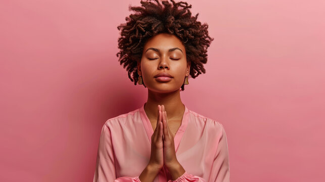 Young Woman With Curly Hair In A Serene Pose With Her Eyes Closed And Hands Together In A Gesture Of Prayer Against A Soft Pink Background