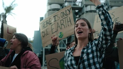 Serious girl with her fist in the air in a demonstration. Group of people at manifestation on climate change and global warming pollution and factories, environmentalists involved in the fight against