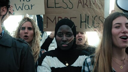 Serious Muslim woman in the middle of a demonstration by a group of activists people holding anti-war banners during a peace and human rights manifestation
