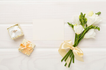 White fresia flower and gift box with diamond ring on wooden background, top view
