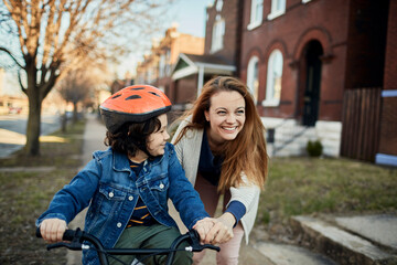 Fototapeta premium Mother teaching child to ride a bicycle in suburb