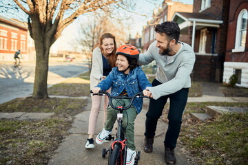 Family teaching child to ride a bicycle in suburban neighborhood