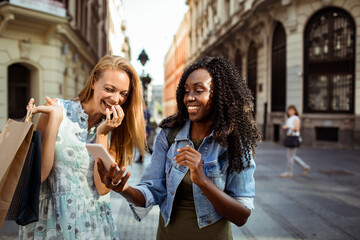 Diverse young women using smartphone and shopping in city