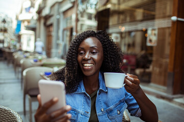 Cheerful Woman Enjoying Coffee and a Video Call at a Sidewalk Cafe