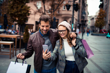 Happy young couple using smartphone while shopping in city