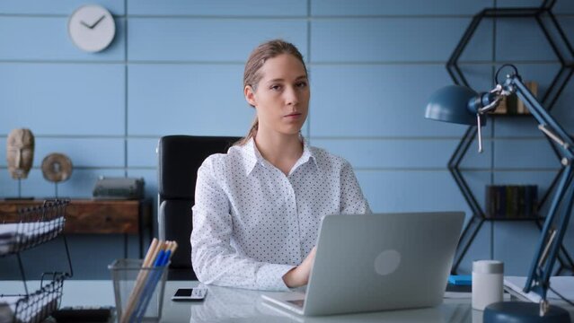 portrait of young woman in white shirt, sitting at table desk in office and working at laptop. types on keyboard focused, looks in camera seriously, turn head in sign of disagree and reject