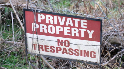 Close up of Private Property No Trespassing warning sign behind a wire fence