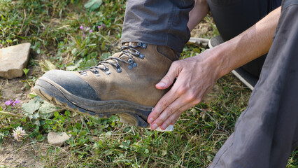 Close-up of a man's hands repairing a torn leather walking boot. The sole of the boot is being...