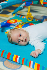 Obraz premium Child development. The baby lies on the developing mat and plays with toys. While playing, the child gets to know the world and learns shapes and colors.