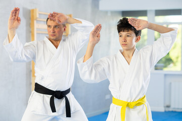 Dynamic underage boy performing fighting positions with middle-aged trainer during karate courses