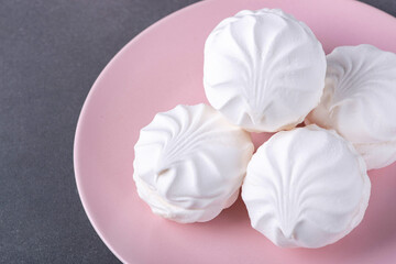 White fluffy marshmallows or marshmallow shells with powdered sugar sprinkles on a pink plate on a...
