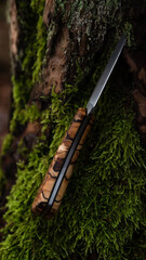 Ein handgeschmiedetes Messer mit einem Griff aus gestockter Birke in einer bewaldeten Kulisse